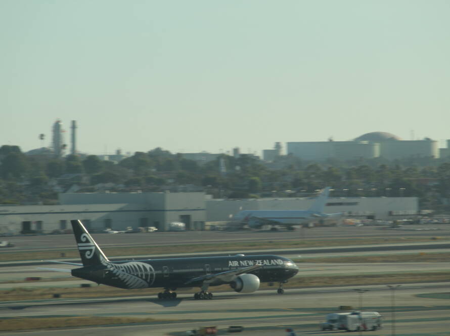 Air New Zealand aircraft taxiing on a runway with black livery and white fern design, preparing for takeoff amid hazy daylight conditions.