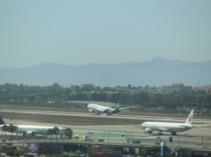 New Zealand aircraft landing with white smoke trailing from rear tires; China Airways jet poised for takeoff on opposite runway at LAX.