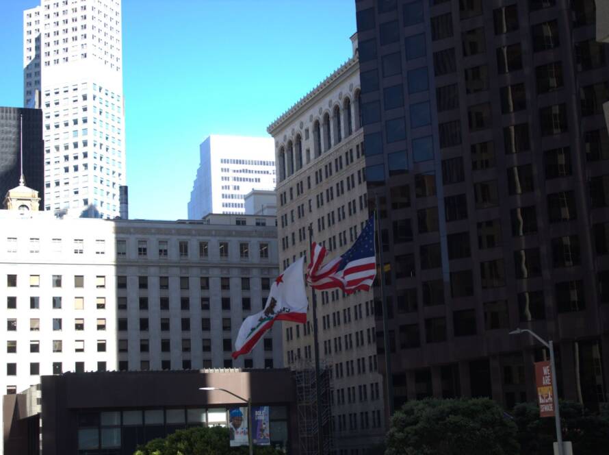 Downtown cityscape with historic and modern buildings and US and California flags, symbolising civic trust and the interplay of legacy operations and modern finance.